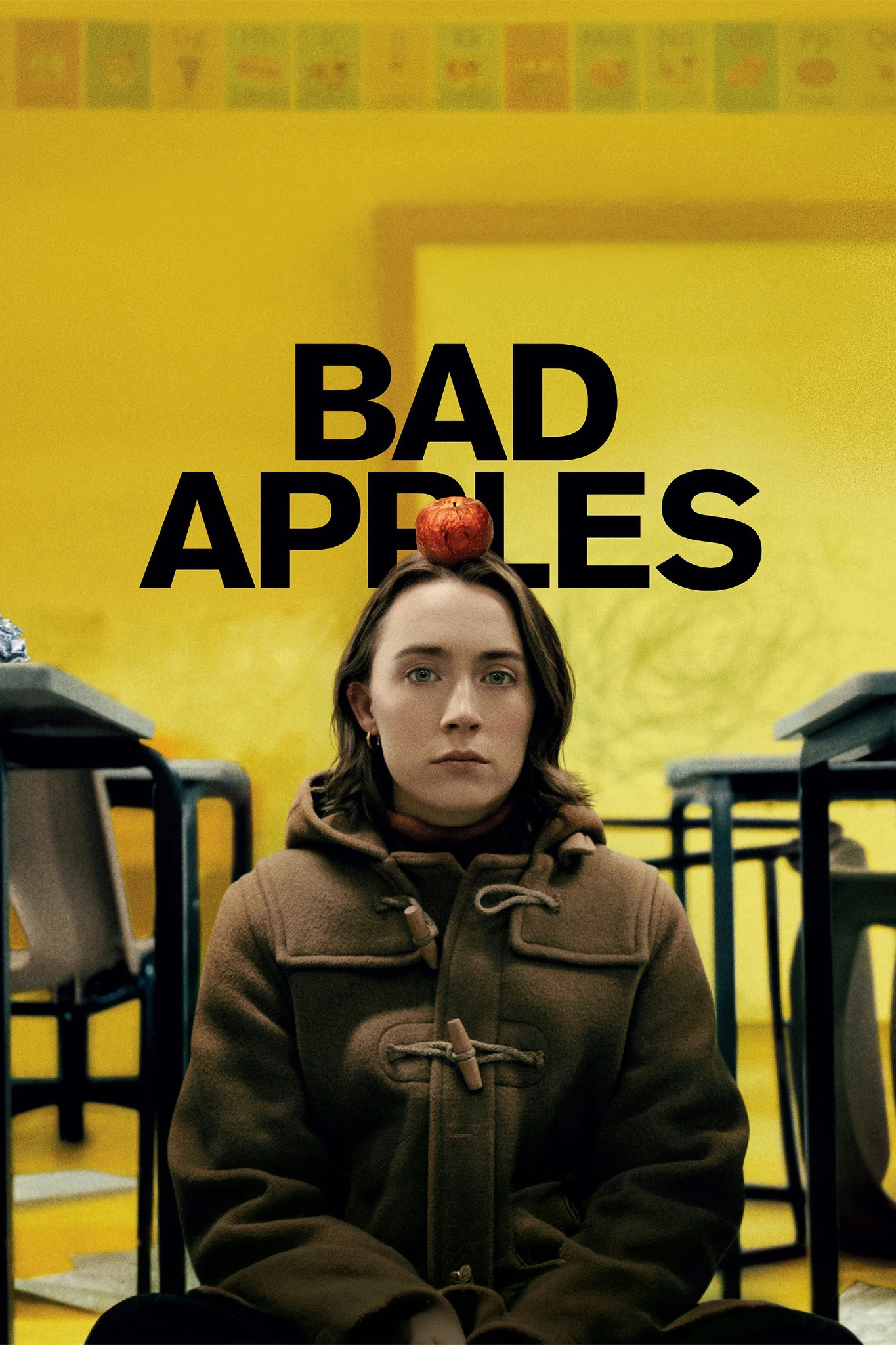 بوستر Bad Apples الأصفر: ماريا تجلس بين طاولات مدرسية، وتفاحة فوق رأسها، والعنوان الأسود الكبير واضح خلفها