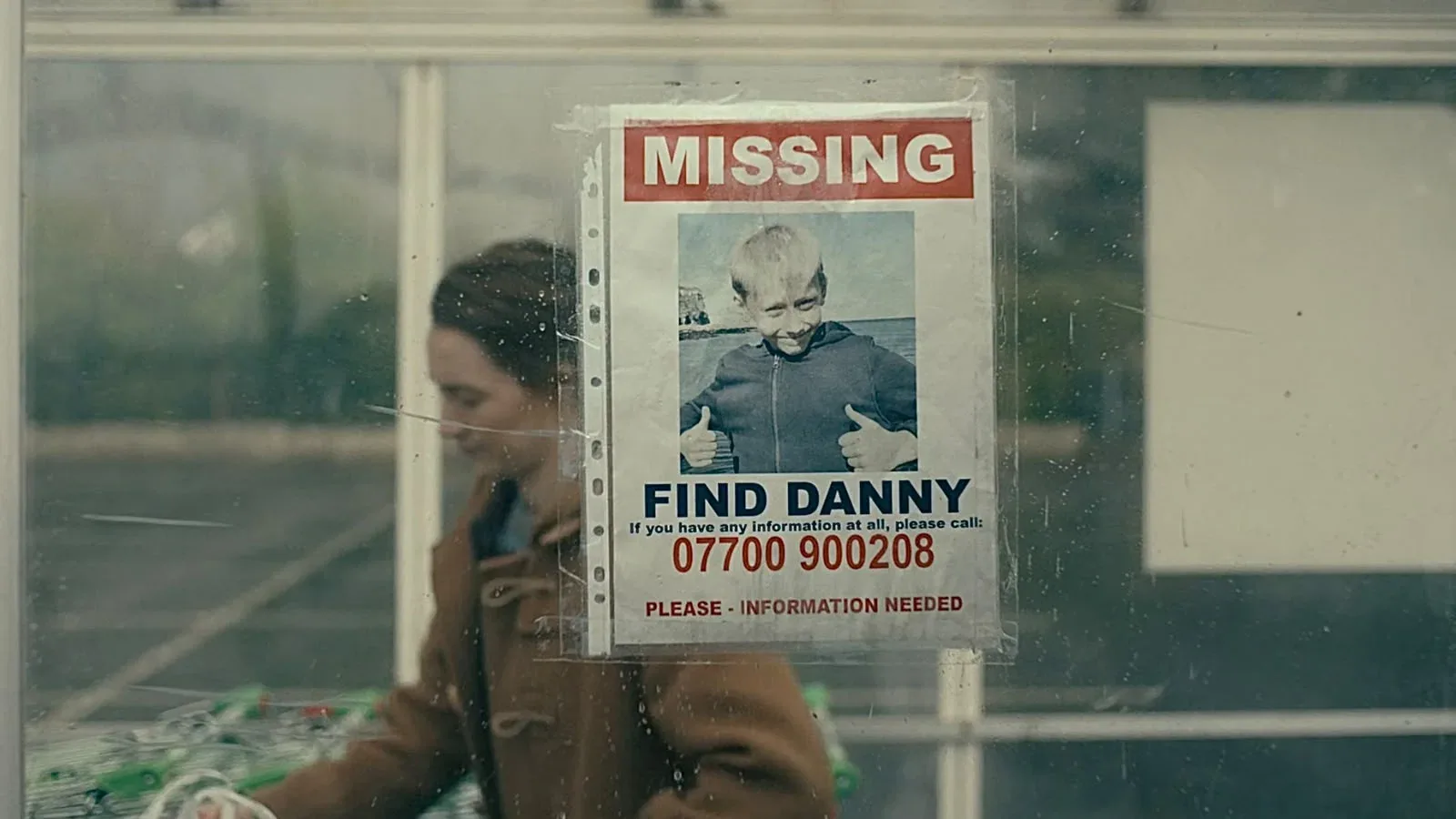 إعلان طفل مفقود بعنوان MISSING وصورته واسم Danny مثبت على زجاج نافذة وشخص يتحرك خلف الإعلان