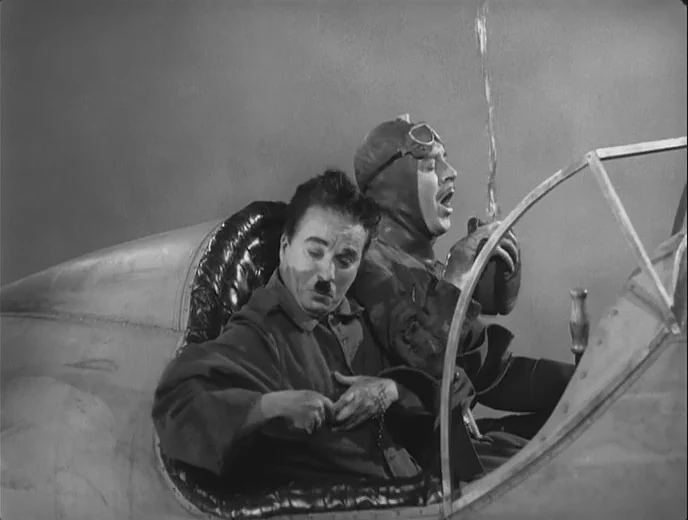 تشابلن وريجنالد غاردنر في مشهد الطائرة من The Great Dictator (1940). تبدأ الحكاية زمن الحرب العالمية الأولى قبل الانتقال إلى عالم الدكتاتور.